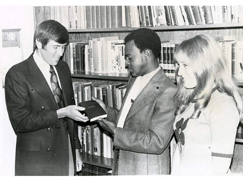 Dean Gary Collins presents Bibles to new students Joseph Gaines and Kay Lewis, circa 1970s. Queenie Simmons Archive, California Baptist University. 