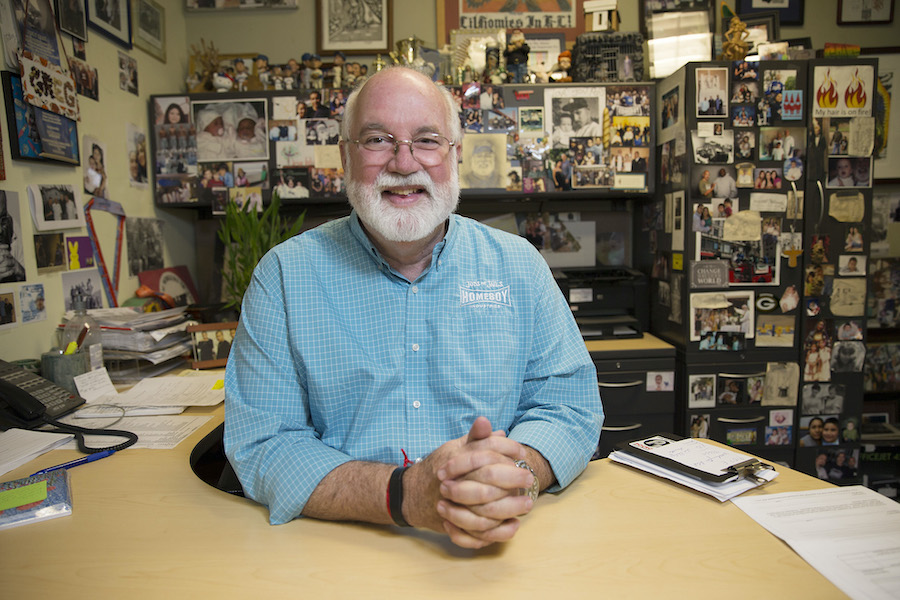 Father Greg Boyle sitting at a desk, smiling