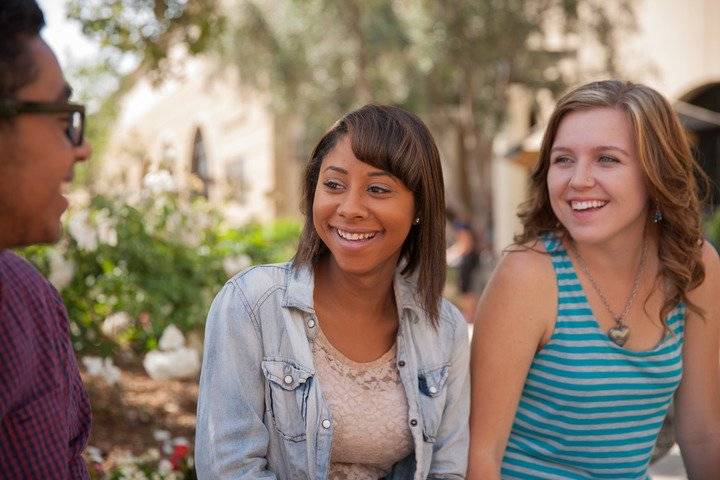 Three smiling CBU students having a conversation outside on campus